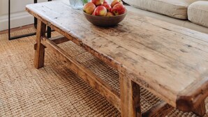 A living room with a wooden table, a vase with flowers, and a bowl of fruit.