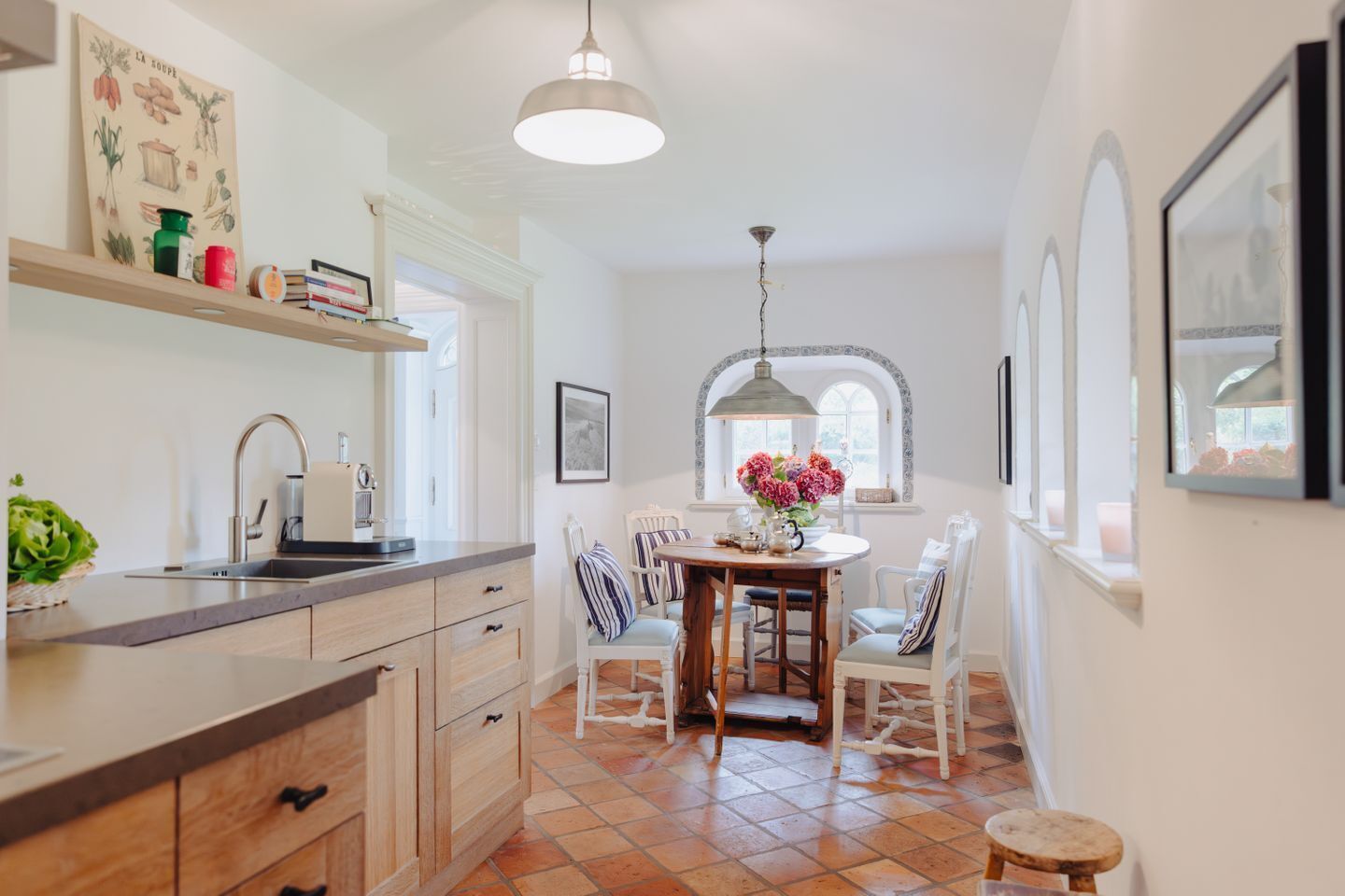 Una cocina con un lavamanos, armarios de madera, una mesa de comedor con sillas y una lámpara colgante.