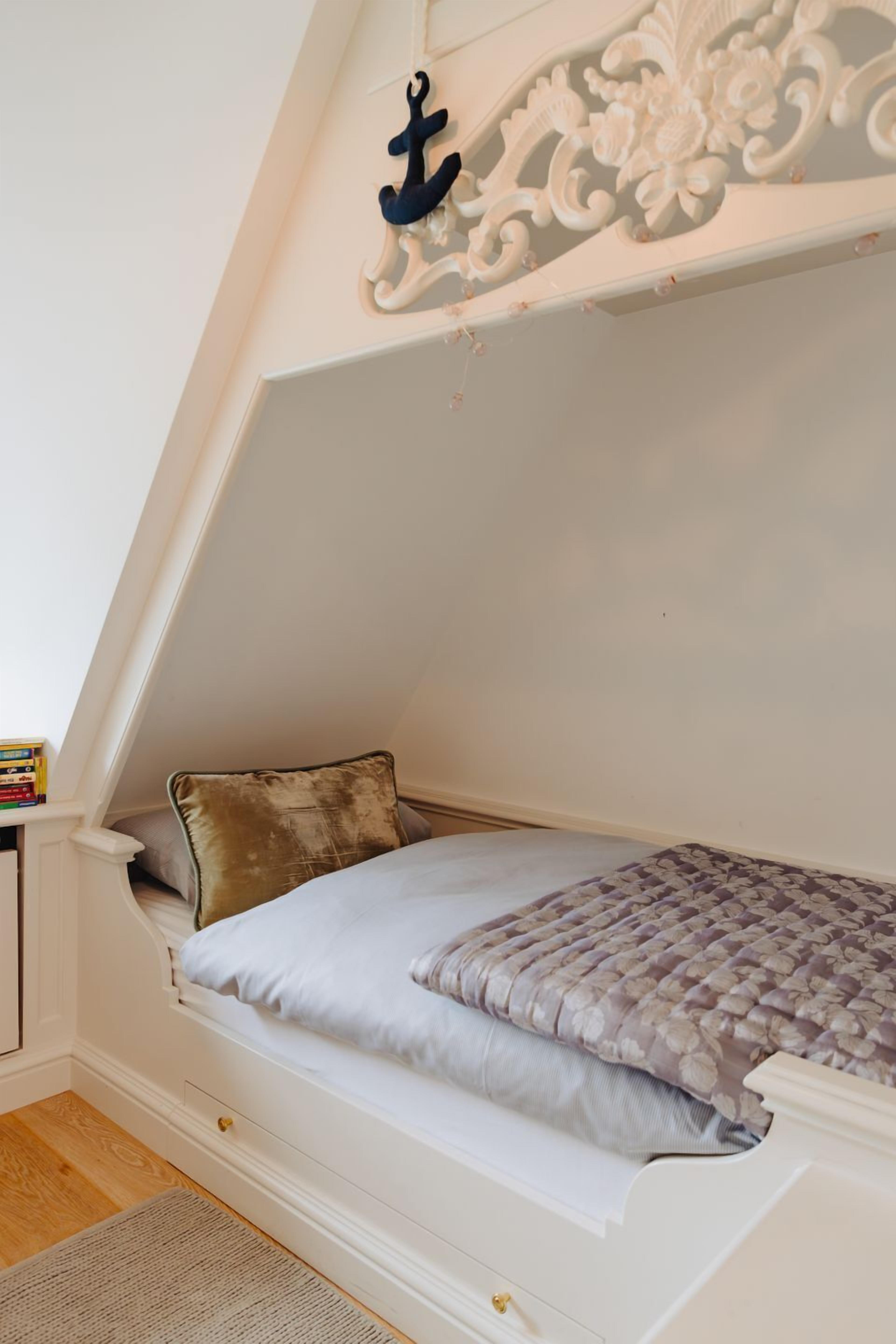 A loft-style bedroom with a sloped ceiling, a decorative anchor, a bed with a patterned bedspread, and a small bedside table with books.