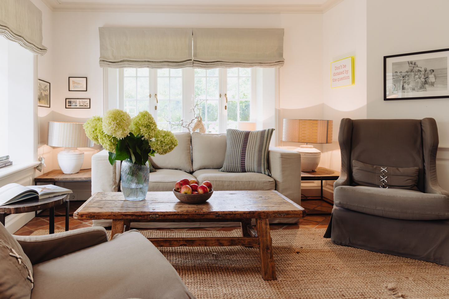 A living room with a sofa, armchair, coffee table, and a vase with flowers.