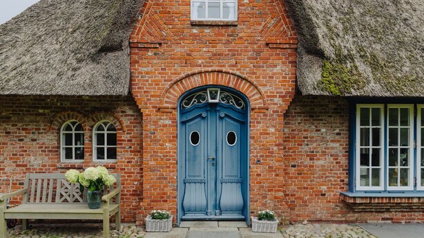 A brick building with a blue door, a bench, and a window with a white frame.