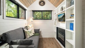 Interior acogedor de una cabaña con techo de madera, chimenea, sofá y estantería.