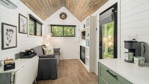 Una cabaña compacta y moderna con techo de madera, paredes blancas y una zona de estar acogedora.