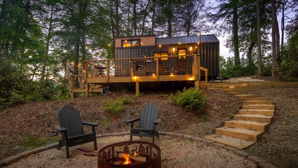 Una cabaña con terraza, un hoyo de fuego y dos sillas Adirondack.