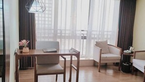 A modern room with a wooden dining table, two chairs, a sofa, and a view through sheer curtains. - Guanhai Holiday Hotel (Lufeng)