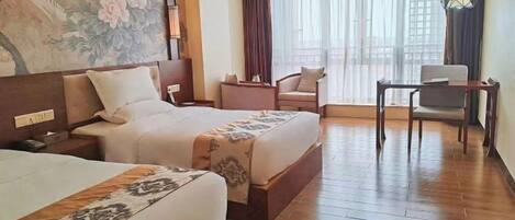 A hotel room with two beds, a desk, a chair, a large window with curtains, and a wall mural.