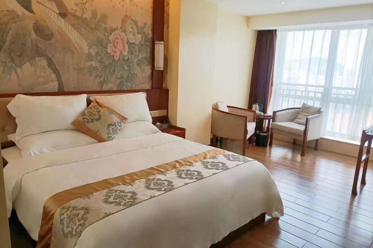 Ein Hotelzimmer mit einem großen Bett, einem Schreibtisch, einem Sessel und Blick ins Freie.