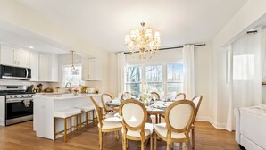 A modern kitchen with white cabinetry, a central island, and a dining area with wooden chairs and a chandelier. - French Country Cottage in lovely Glen Ellyn! (Glen Ellyn)