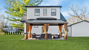 A two-story house with a covered patio area featuring outdoor furniture and curtains. - French Country Cottage in lovely Glen Ellyn! (Glen Ellyn)