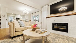 A living room with a beige sofa, a round coffee table, a fireplace, and a television mounted on the wall. - French Country Cottage in lovely Glen Ellyn! (Glen Ellyn)