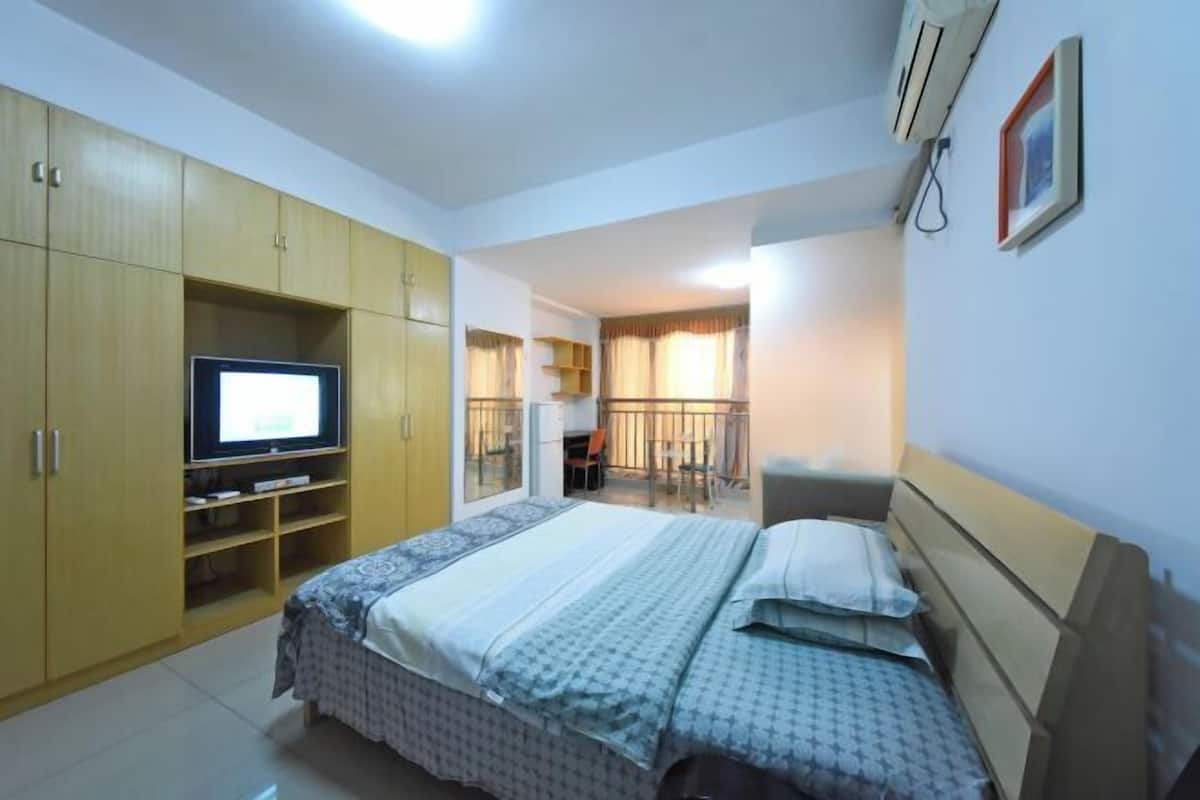 A bedroom with a bed, a TV, a wardrobe, and a balcony with a railing.