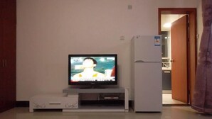 A room with a television on a stand, a refrigerator, and a door leading to another room. - Qinqinwojia Apartment (Changsha Dongyi International) (Changsha)