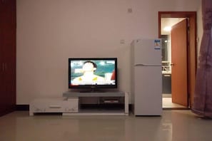 A room with a television on a stand, a refrigerator, and a door leading to another room. - Qinqinwojia Apartment (Changsha Dongyi International) (Changsha)