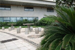 A building with a tiled exterior, outdoor seating area with tables and chairs, and a palm tree.