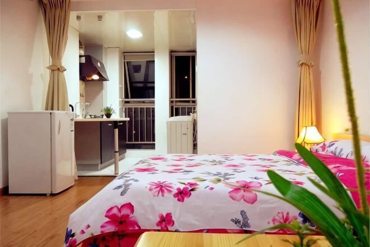 A bedroom with a bed, a desk, a refrigerator, and a balcony.