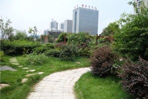 Un camino serpentea por un jardín ajardinado, con un paisaje urbano al fondo.
