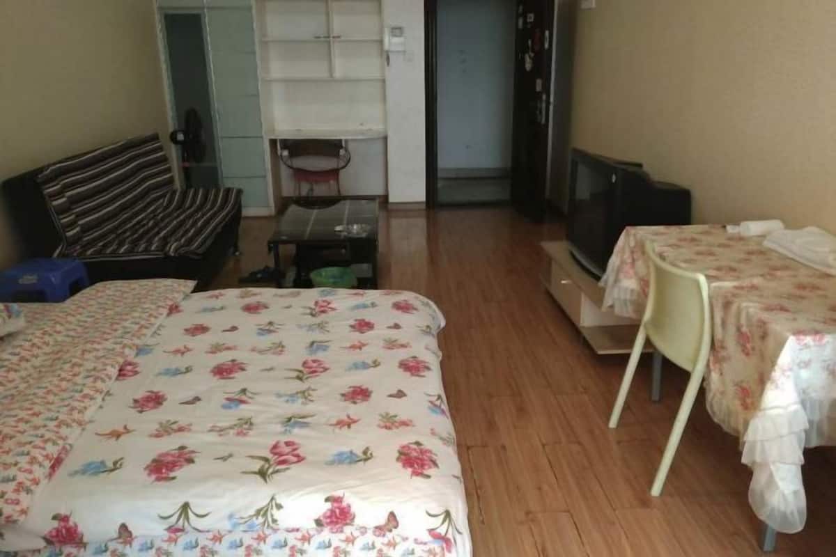 A hotel room with a bed, a television, a small table, a chair, and a door leading to a hallway.