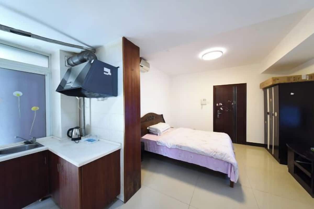 A bedroom with a bed, a desk with a lamp, a wardrobe, and a TV.