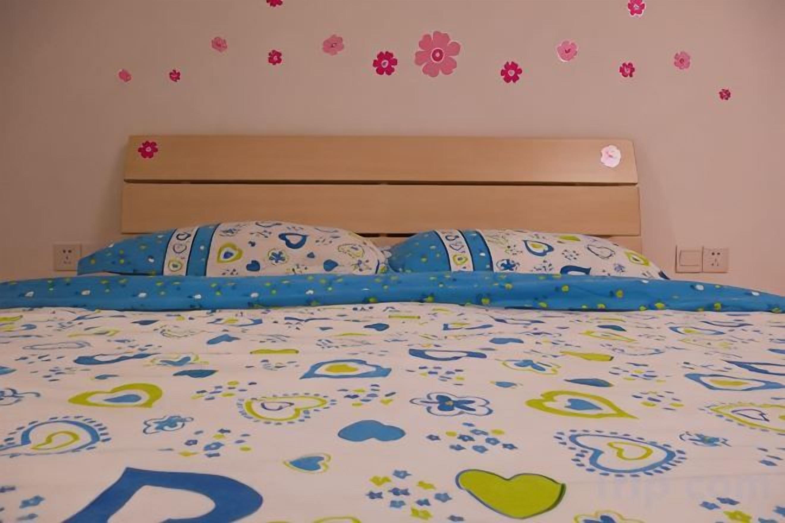 A bed with a patterned bedspread, pillows with a paisley design, and a wall with flower decals.