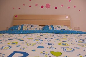 A bed with a patterned bedspread, pillows with a paisley design, and a wall with flower decals.