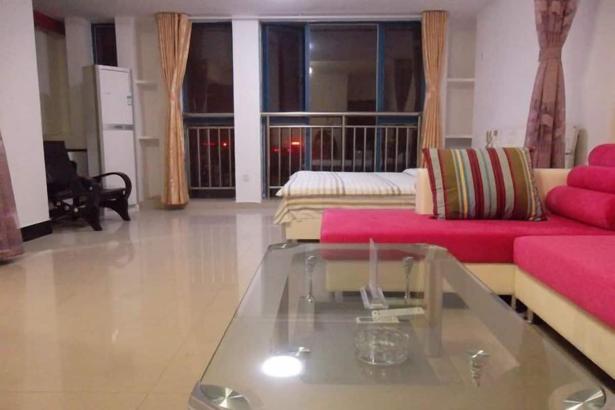 A living room with a glass coffee table, a red sofa, a white sofa, and a bed with striped pillows.