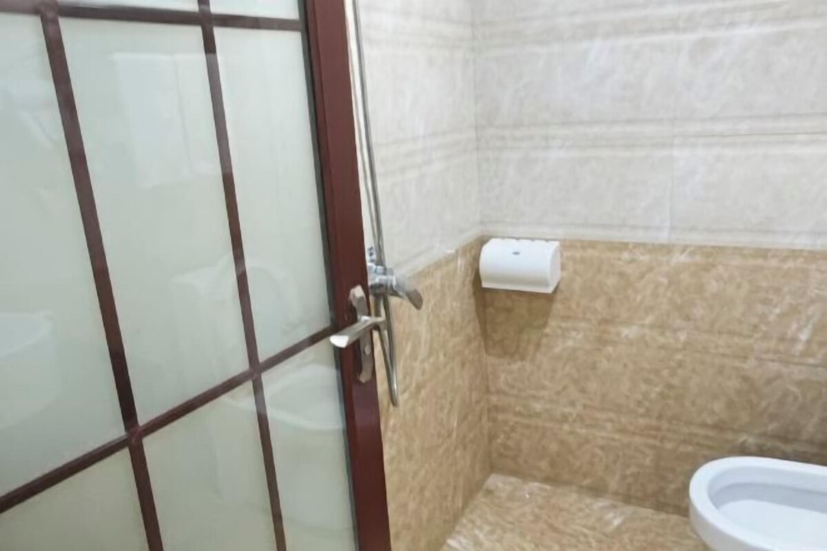 Casa de banho com sanita, dispensador de papel e porta de vidro com puxador de metal.