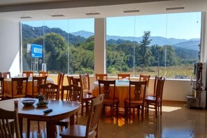 Un área de comedor con mesas y sillas, ventanas amplias con vistas a montañas, y un letrero con caracteres chinos.