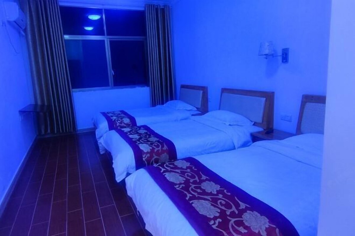 Quarto de hotel com duas camas, uma janela com cortinas, uma luminária na parede e piso revestido de azulejos.