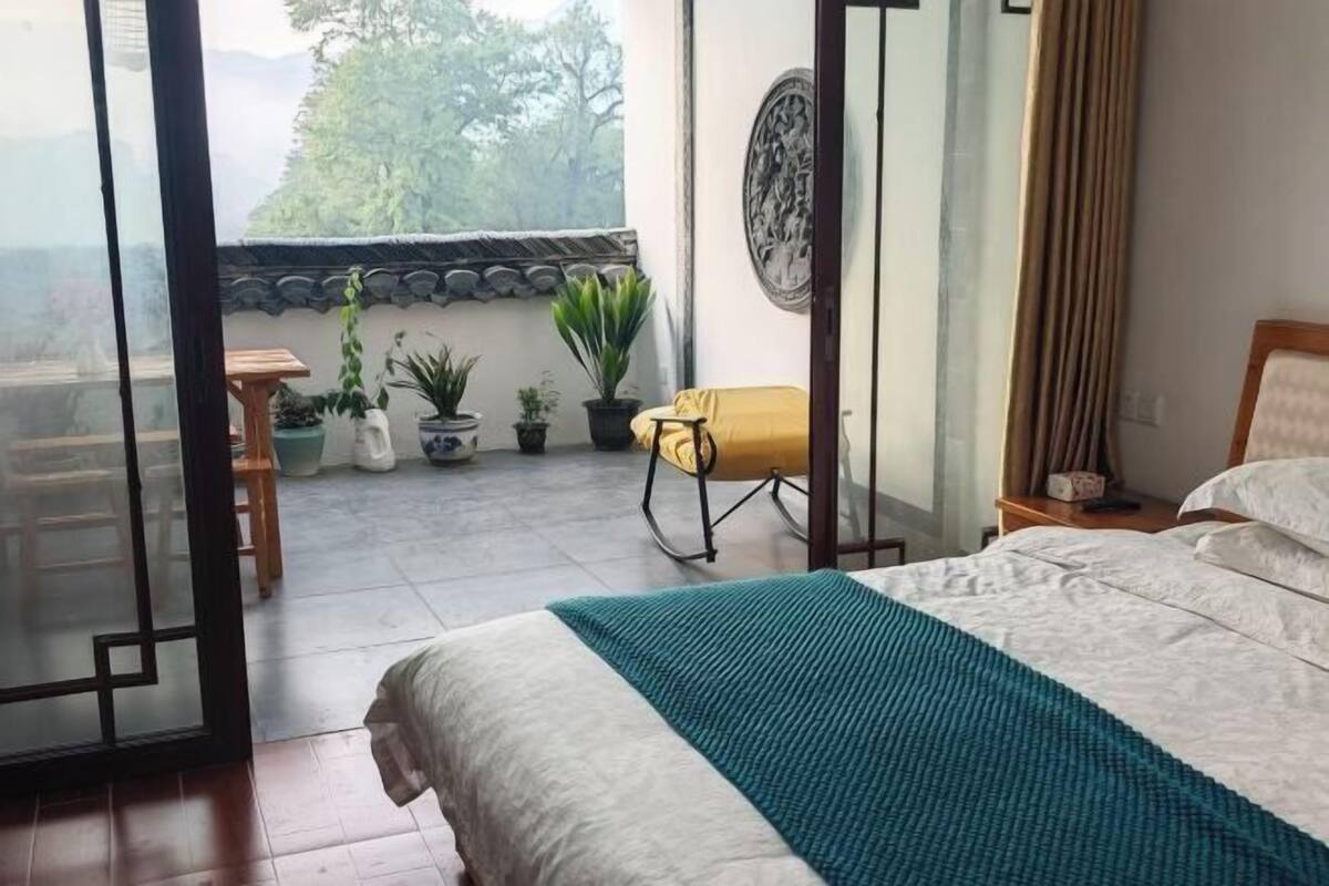 Un dormitorio con una cama, una silla amarilla y vistas a un balcón con plantas.