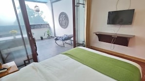 Ett hotellrum med en säng, en tv som är monterad på väggen och en balkong med en stol och växter.