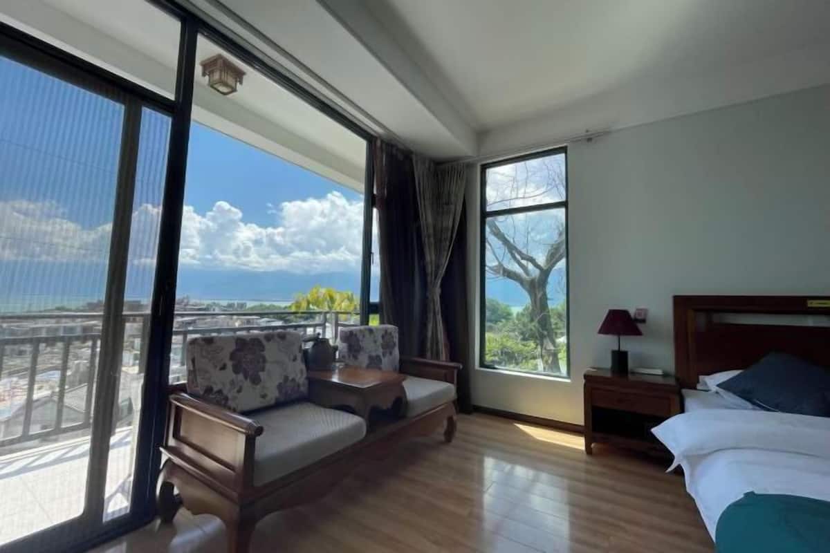 A hotel room with a large window, a sofa, a bed, and a nightstand.