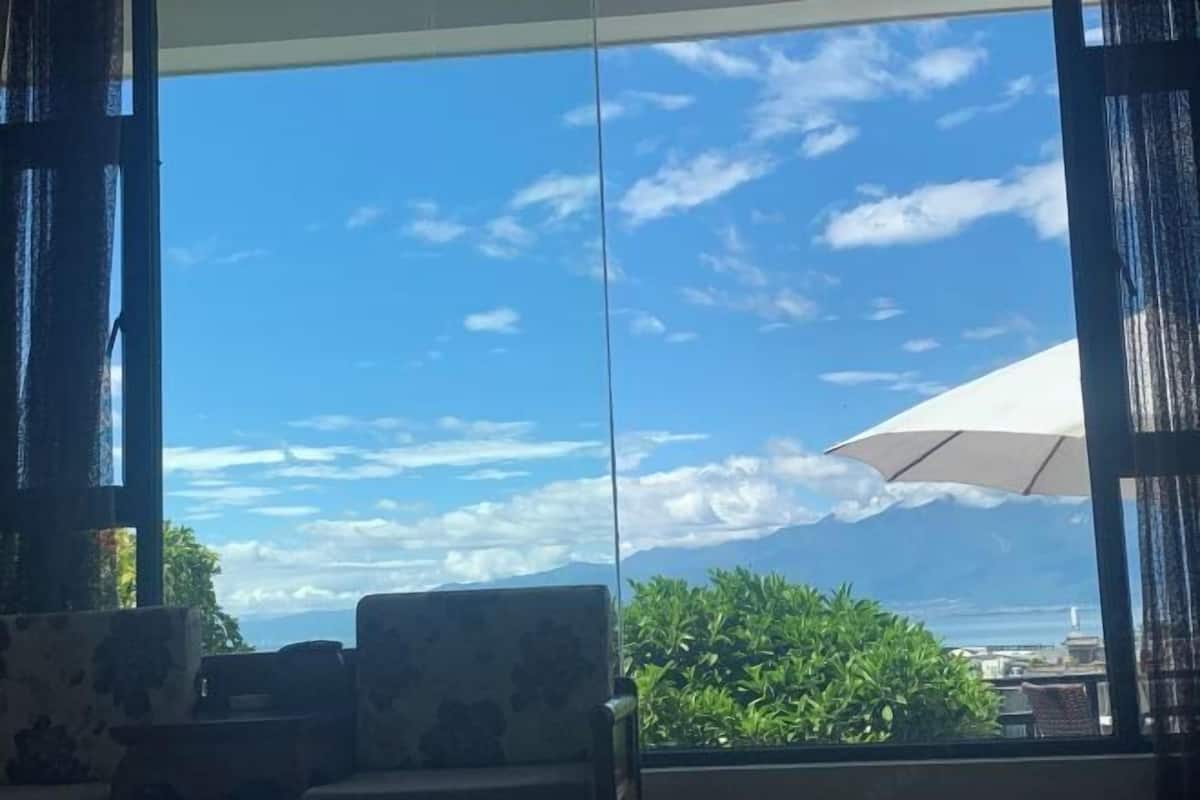 A room with a large window, a view of the sky, and a white umbrella.