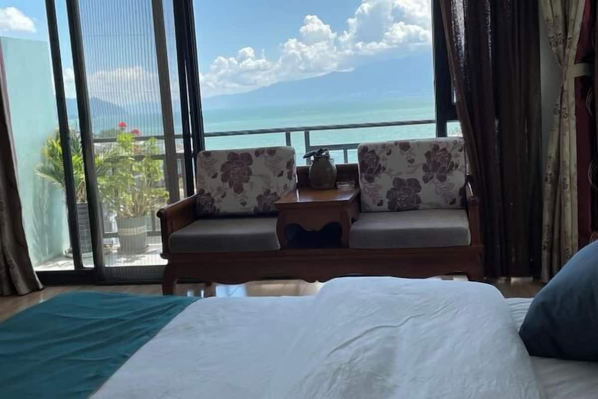 A room with a bed, two upholstered chairs, a small table, and a view of the ocean.