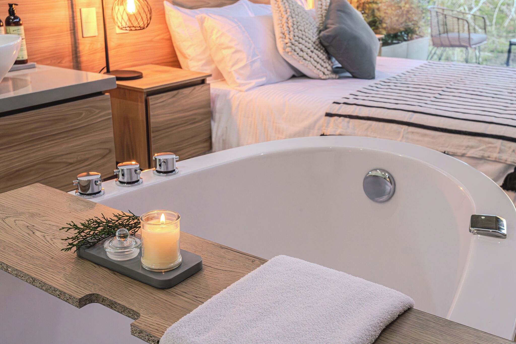 Ein modernes Badezimmer mit Badewanne, Holzwaschtisch, einer brennenden Kerze und einem Handtuch.