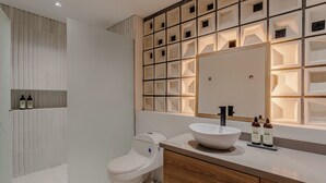 Un bagno moderno con un water bianco, un lavandino grande e uno specchio sopra. Sul piano del lavandino ci sono due bottiglie.
