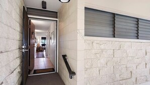 A hallway with a door leading to a room, a window with blinds, and a textured wall.