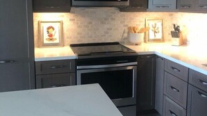 A modern kitchen with dark cabinets, a microwave, a stove, and a dishwasher. There are framed pictures on the wall and a knife block on the counter.