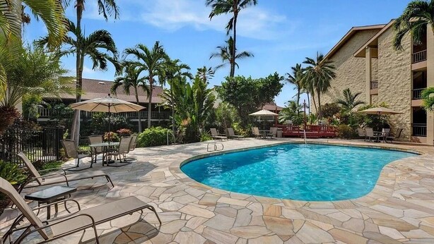 A pool area with stone flooring, lounge chairs, and umbrellas.