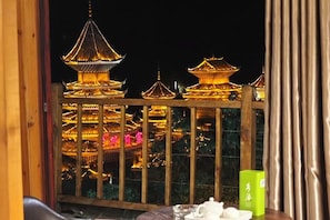 A view of traditional pagoda-style buildings at night, viewed through a window with a wooden railing.
