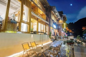 A wooden building with balconies and large windows, a patio with outdoor seating, and a night sky.
