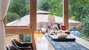 A room with a wooden table set with tea utensils, a patterned table runner, and a view of lush greenery outside. - Zhaoxing Dong Village at that time, flowers blossoming, live music, courtyard homestay (Liping)