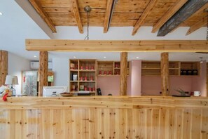 A wooden interior with a reception desk, shelves with red containers, and a pink wall.