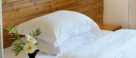 Una cama con sábanas blancas, cabecera de madera y un florero sobre la mesita de noche.