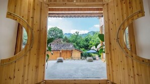 A wooden-framed doorway leading to an outdoor area with a traditional building and greenery in the background. - Zhaoxing Dong Village at that time, flowers blossoming, live music, courtyard homestay (Liping)