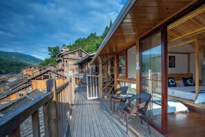 Una terraza de madera con una habitación con paredes de vidrio, una cama y una silla.