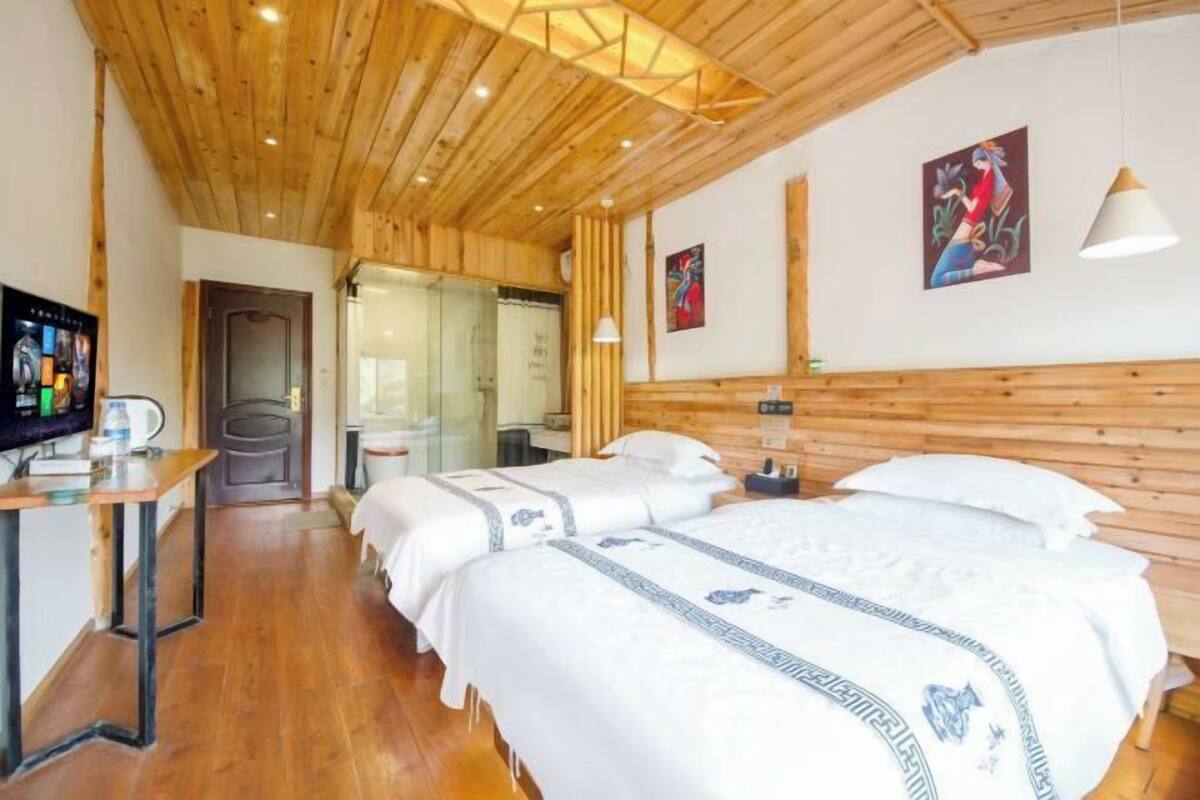 Hotellihuone, jossa on puinen katto, kaksi sänkyä valkoisilla vuodevaatteilla, työpöytä tietokoneella ja televisio.