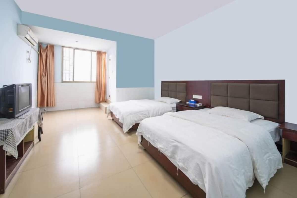 A hotel room with two beds, a television, and a window with curtains.