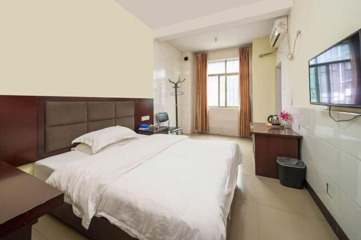 A hotel room with a bed, a desk, a chair, a TV, and a window.