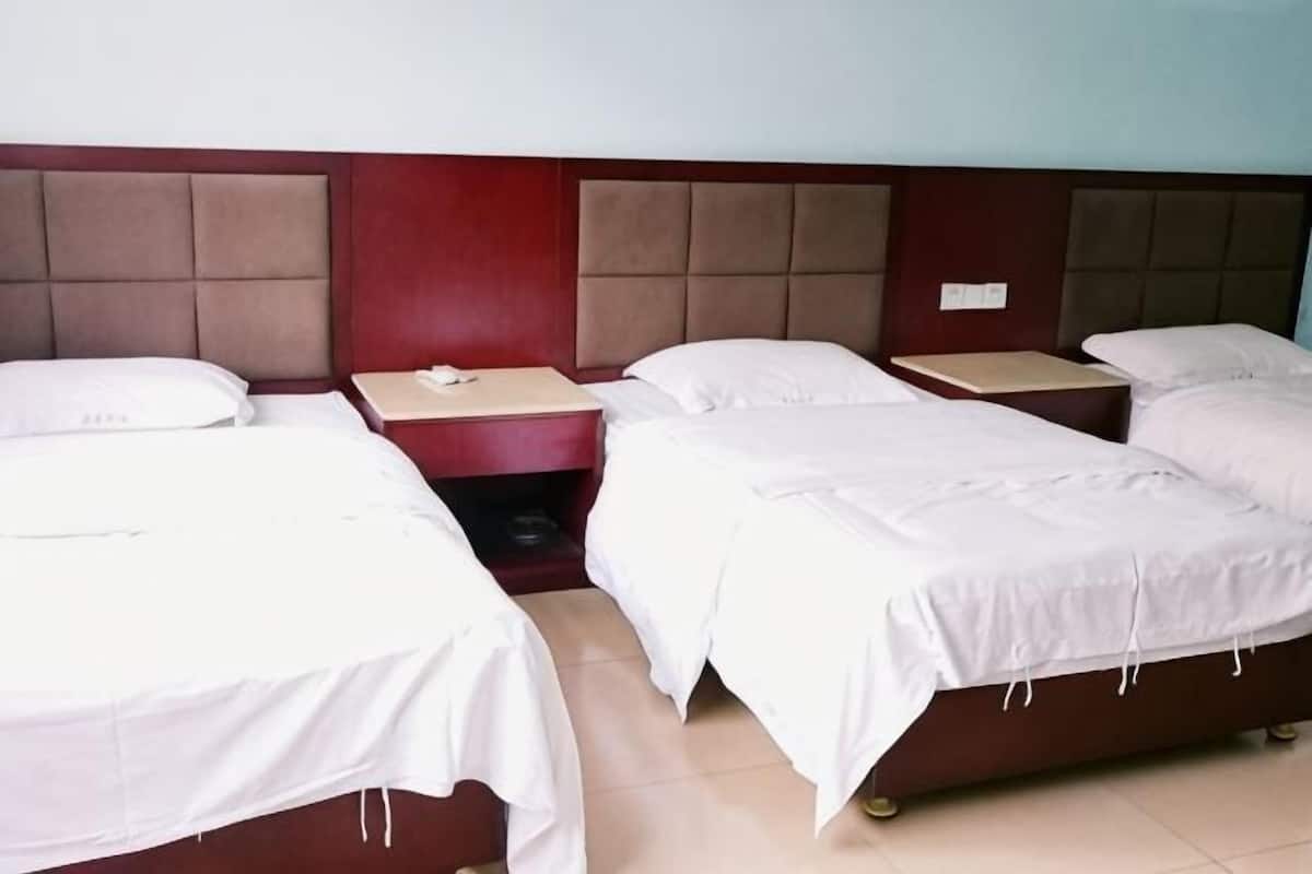 A hotel room with four single beds, a wooden headboard, and a small bedside table with a lamp.