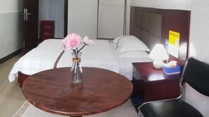 A hotel room with a bed, a small round wooden table with a vase of flowers, a desk with a lamp, and a chair. - Chenzhou Junhao Hotel (Chenzhou)